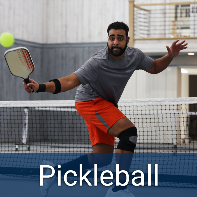 adult male hitting a pickleball with paddle on an indoor pickleball court, header reads "Pickleball"