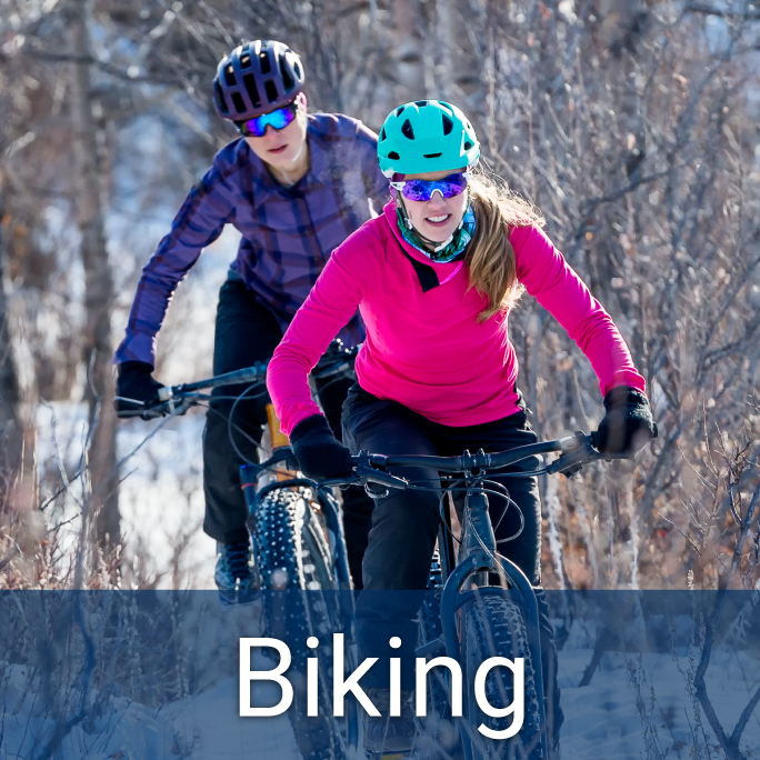 Two adults bike through snow-covered forest in winter, header reads "Biking"